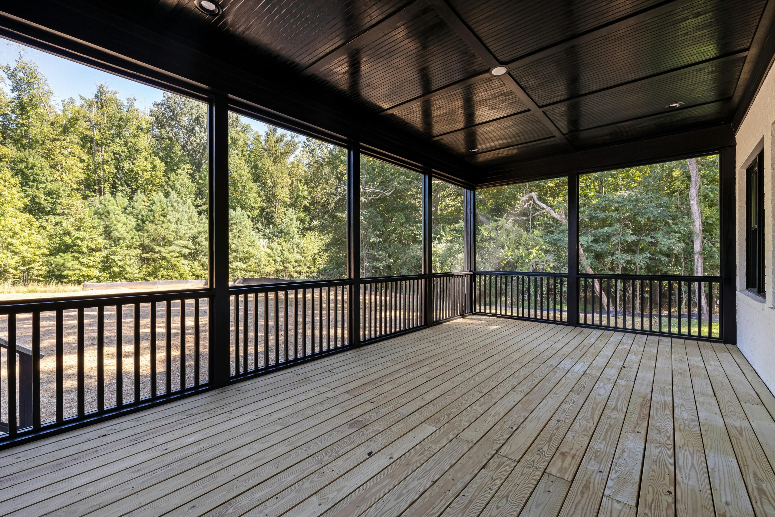 A large wooden patio with a serene view of lush green forest surroundings.
